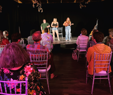 Three people standing stage in front of crowd